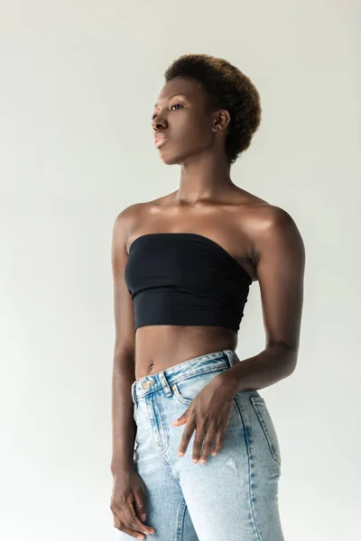 Hermosa chica afroamericana en jeans y top negro aislado en gris - foto de stock