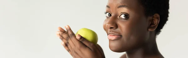 Foto panorámica de la feliz mujer afroamericana sosteniendo manzana verde aislada en gris - foto de stock