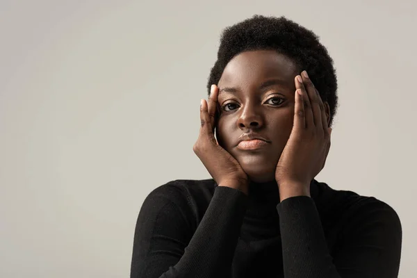 Mujer afroamericana trastornada en cuello alto negro aislada en gris - foto de stock