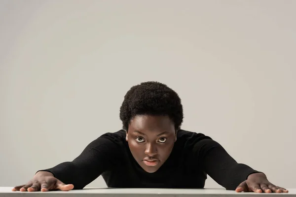 African american woman in black turtleneck sitting at table isolated on grey — Stock Photo