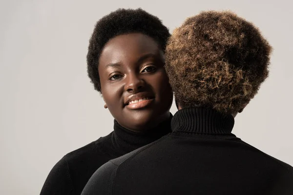 Souriant afro-américaine filles en noir col roulé câlin isolé sur gris — Photo de stock