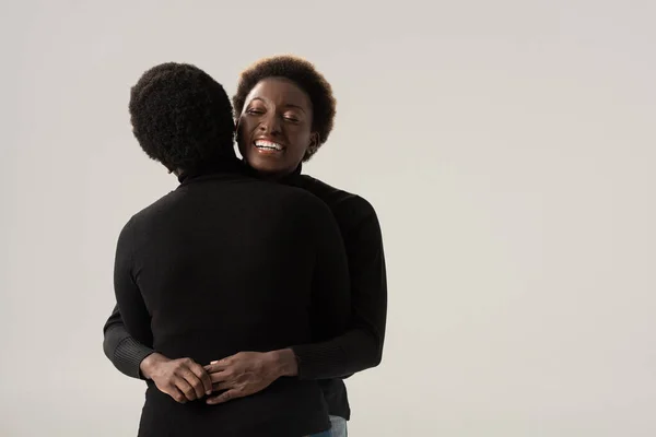 Alegre afro-americana namoradas em golas pretas abraçando isolado no cinza — Fotografia de Stock