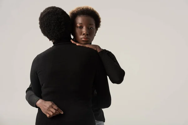 Chicas afroamericanas atractivas en cuellos altos negros abrazándose aisladas en gris - foto de stock