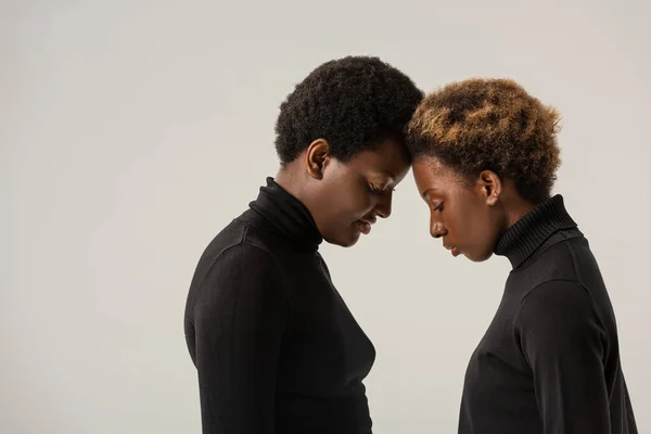 African american women in black turtlenecks touching foreheads isolated on grey — Stock Photo