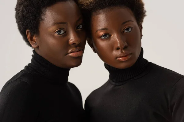 Hermosas mujeres afroamericanas en cuellos altos negros aisladas en gris - foto de stock