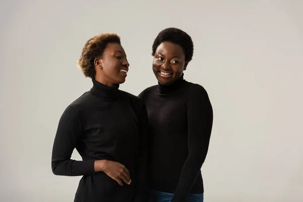 Cheerful african american friends in black turtlenecks hugging isolated on grey — Stock Photo