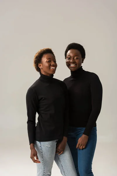 Smiling african american friends in black turtlenecks hugging isolated on grey — Stock Photo