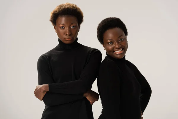 Sorridenti amiche afro-americane in dolcevita nero con braccia incrociate isolate su grigio — Foto stock