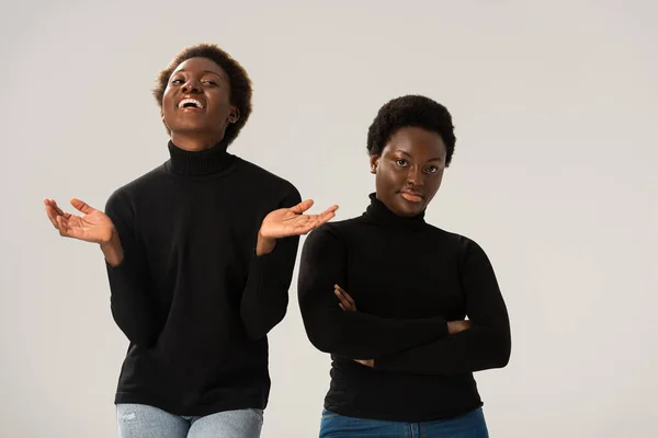 Смеющиеся африканские американские девушки в черных водолазках со скрещенными руками, изолированными на сером — стоковое фото