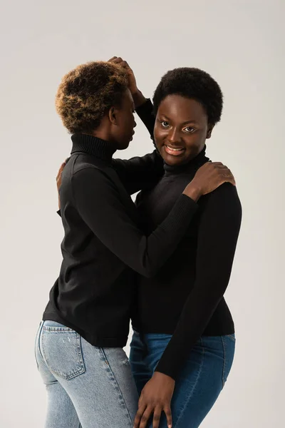 Smiling african american women in black turtlenecks hugging isolated on grey — Stock Photo