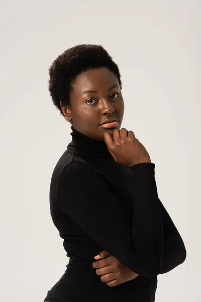 Durchdachte attraktive afrikanisch-amerikanische Frau in schwarzem Rollkragen isoliert auf grau — Stockfoto