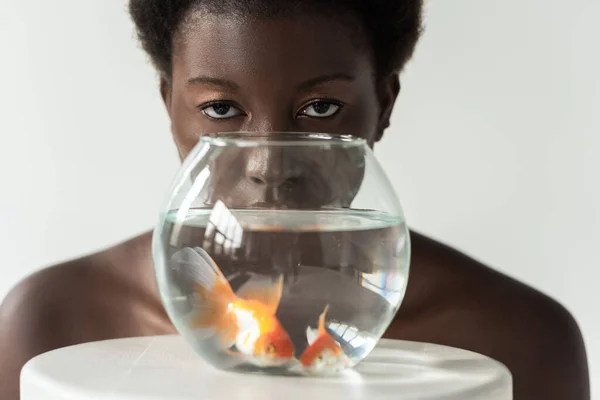 Оголена афроамериканська дівчина дивиться через акваріум з рибою ізольовано на сірому — стокове фото