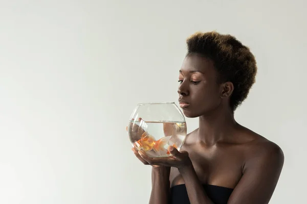 Atractiva chica afroamericana sosteniendo acuario con peces aislados en gris - foto de stock