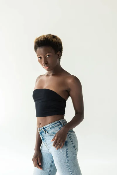 Красивая африканская американка в джинсах и черном топе, изолированная на сером — стоковое фото