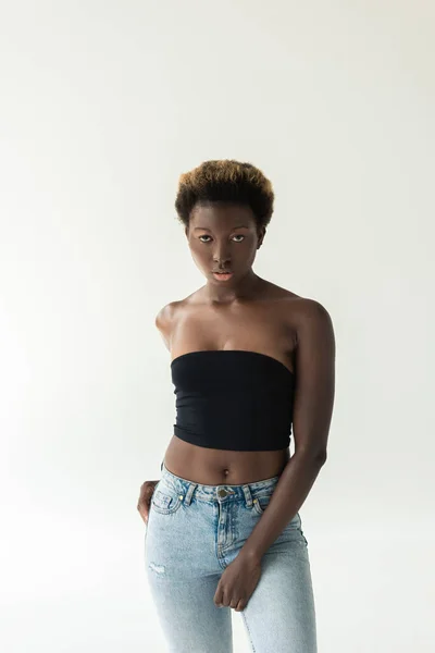 Atractiva chica afroamericana en jeans y top negro aislado en gris - foto de stock