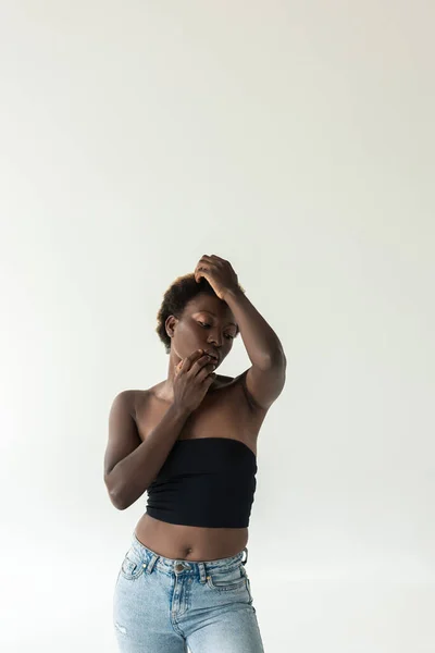 Tender african american girl in jeans and black top isolated on grey — Stock Photo