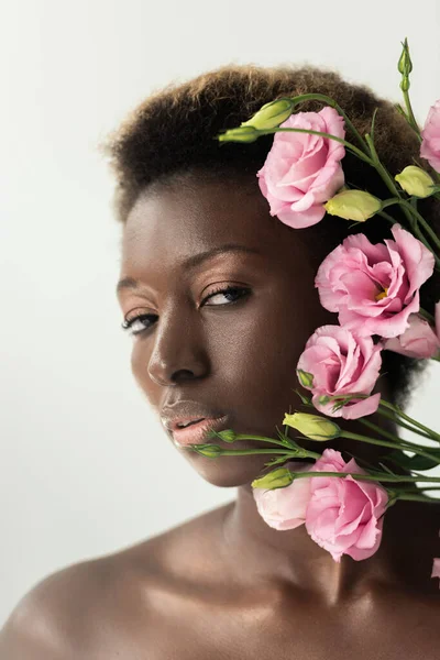 Atractiva chica afroamericana desnuda con flores de eustoma rosa aisladas en gris - foto de stock