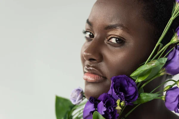 Hermosa mujer afroamericana con flores de eustoma púrpura aisladas en gris - foto de stock