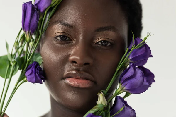 Atractiva mujer afroamericana con flores de eustoma púrpura aisladas en blanco - foto de stock