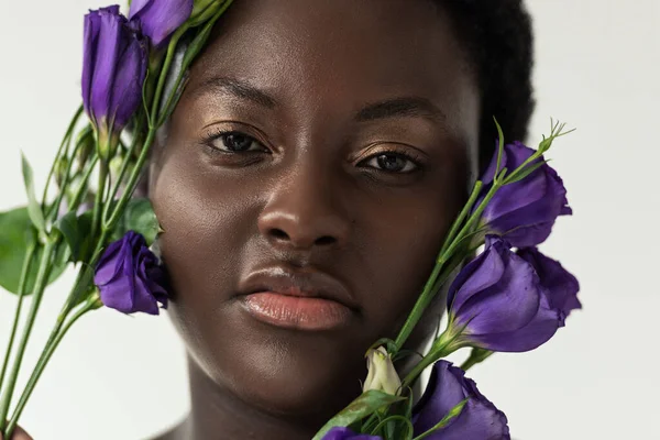 Attractive african american woman with purple eustoma flowers isolated on white — Stock Photo