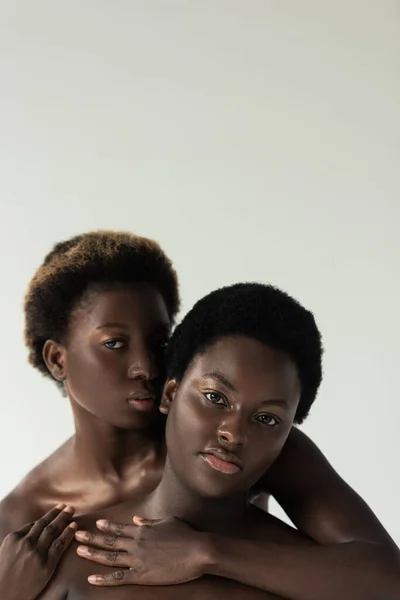 Красиві оголені афроамериканські друзі обіймаються і дивляться на камеру ізольовано на сірому — стокове фото
