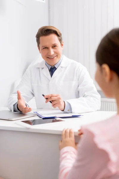 Sonriente ent médico hablando con el niño durante la consulta - foto de stock