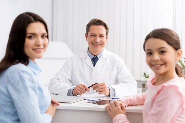 Happy otolaryngologist and mother with daughter smiling at camera during consultation — Stock Photo