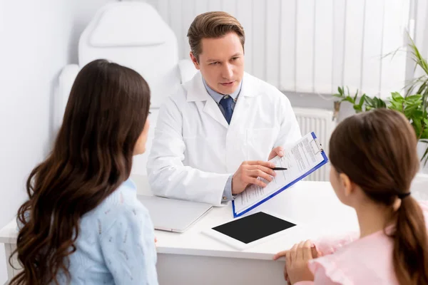 Back view of mother and daughter looking at ent physician showing clipboard with prescription — Stock Photo