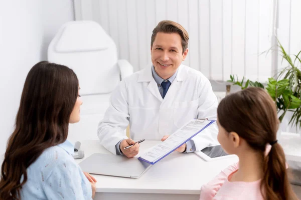 Vista posterior de la madre y la hija mirando ent médico mostrando portapapeles con receta - foto de stock