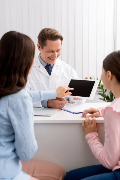 Назад вид матери и дочери рядом с врачом показывая цифровые таблетки с чистым экраном — стоковое фото