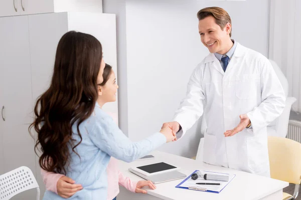 Sonriente ent médico estrechando las manos mientras que la bienvenida madre e hija - foto de stock