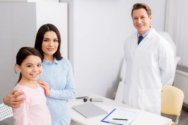 Smiling ent physician and happy mother with daughter smiling while looking at camera — Stock Photo