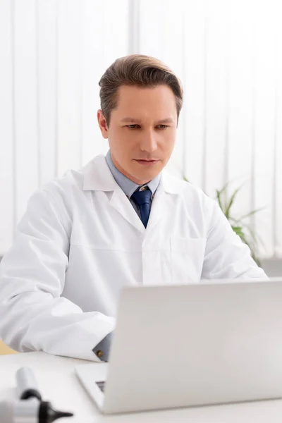 Foyer sélectif de l'otolaryngologue réfléchi en utilisant un ordinateur portable au travail — Photo de stock