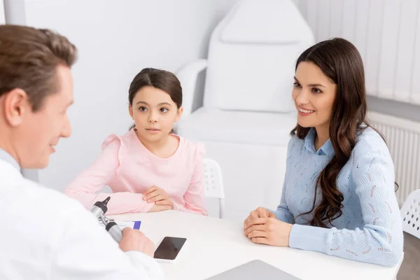 Улыбающаяся женщина с милой дочерью на консультации с врачом — стоковое фото