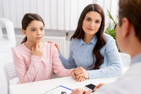 Vista ritagliata di otorinolaringoiatra e donna sorridente che si tiene per mano la figlia che si tocca la gola — Foto stock