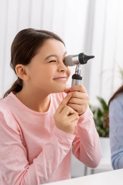 Bambino carino sorridente mentre guarda attraverso l'otoscopio in clinica — Foto stock