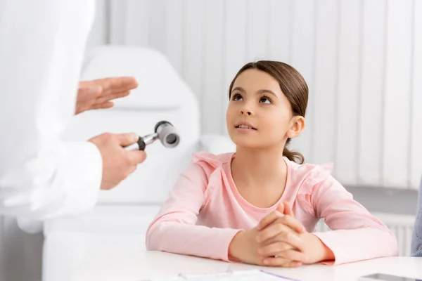 Vista ritagliata del medico ent mostrando otoscopio al bambino carino attento — Foto stock