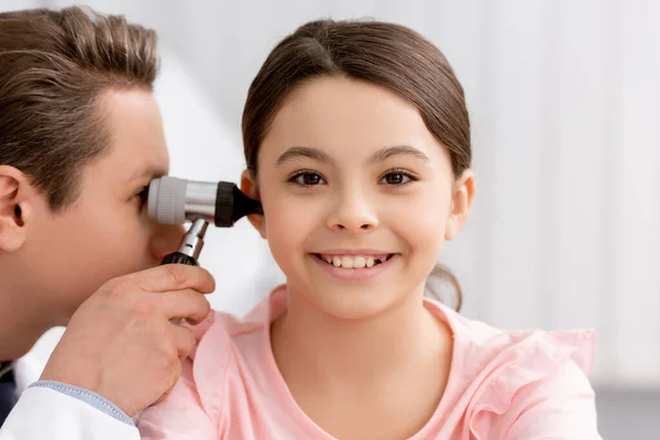 Врач осматривает ухо веселого ребенка с помощью отоскопа — стоковое фото