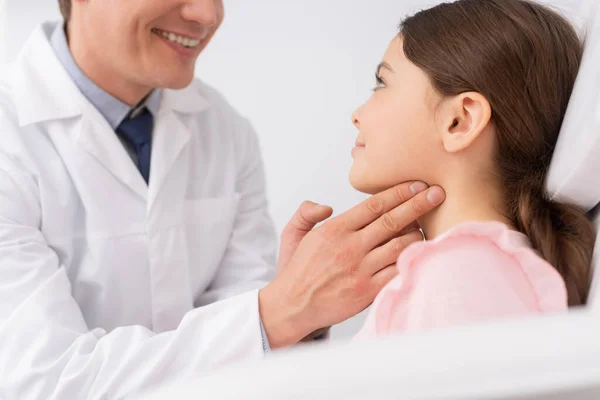 Обрізаний вид усміхненого лікаря, який торкається шиї милої дитини, досліджуючи її горло — стокове фото