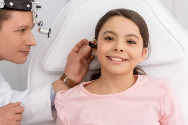 Médecin attentif examinant l'oreille d'un enfant souriant avec spéculum auriculaire — Photo de stock