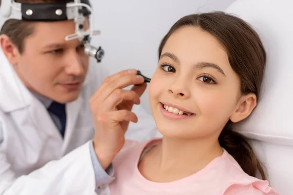 Aufmerksame Ärztin untersucht Ohr eines lächelnden Kindes mit Ohrspekulum — Stockfoto