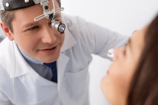 Selective focus of attentive otolaryngologist in ent headlight examining patient — Stock Photo