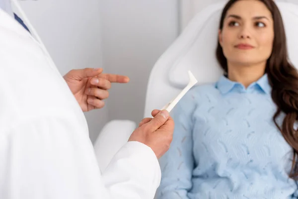 Visão parcial do otorrinolaringologista mostrando espéculo nasal para atraente paciente sentado em cadeira médica — Fotografia de Stock