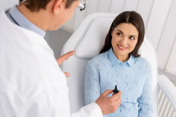 Vue recadrée d'un otolaryngologue tenant un spéculum auriculaire près d'une femme souriante assise sur une chaise médicale — Photo de stock
