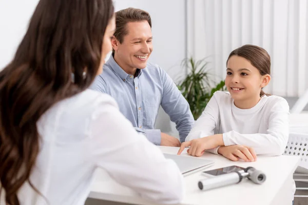 Selective focus of ent physician looking at smiling chid sitting near father during consultation — Stock Photo