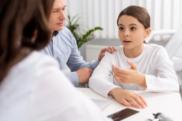 Selektiver Fokus des süßen Kindes, das mit dem Arzt spricht, während es in der Nähe des Vaters sitzt — Stockfoto