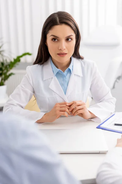 Enfoque selectivo del atractivo médico sentado en el lugar de trabajo - foto de stock