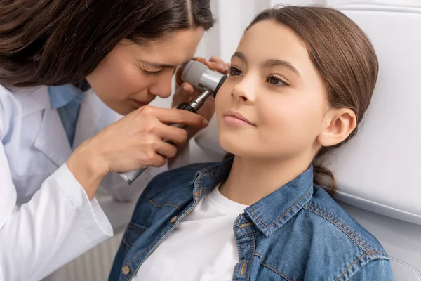 Attentive otolaryngologist examining ear of adorable smiling child with otoscope — Stock Photo