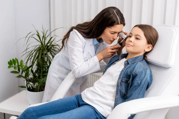 Attentive otolaryngologist examining ear of cute child with otoscope — Stock Photo
