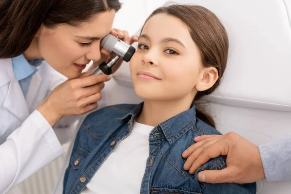 Abgeschnittene Ansicht des Vaters, der die Schulter seiner lächelnden Tochter berührt, während der HNO-Arzt das Ohr untersucht — Stockfoto